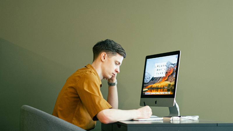 Jeune homme concentré prenant des notes devant un iMac