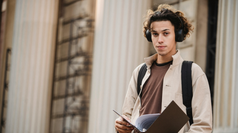 Jeune homme avec un casque audio et un sac à dos feuilletant un document