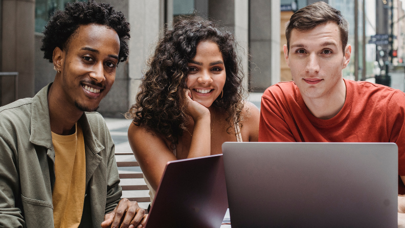 Trois jeunes souriants réunis derrière un ordinateur portable