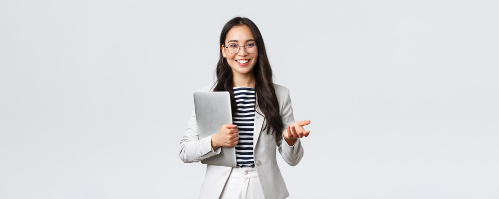 Jeune femme souriante en blazer blanc tenant une tablette sur fond gris clair