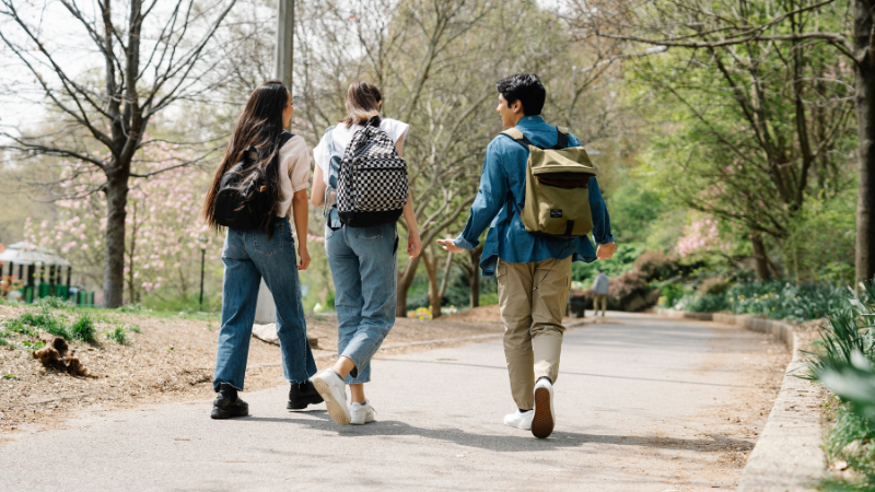 Trois étudiants avec des sacs à dos marchant sur un chemin dans un parc