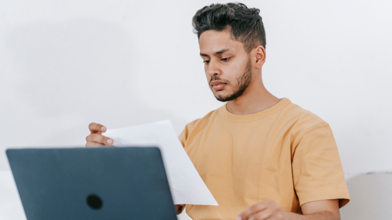 Jeune homme lisant un document devant son ordinateur portable