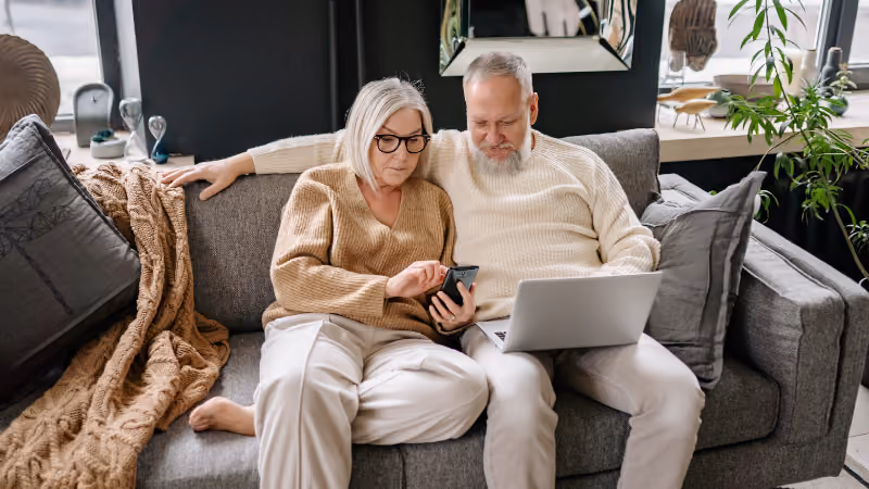 Couple de retraités sur un canapé avec un ordinateur portable et un smartphone