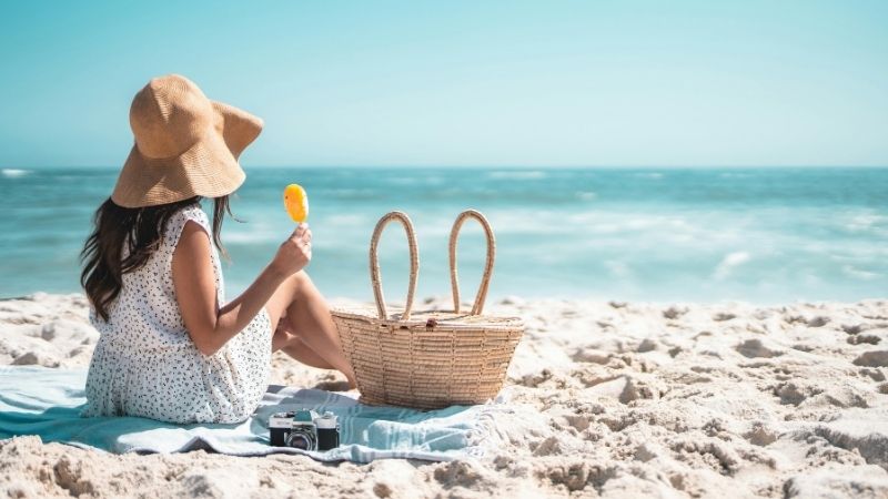 Femme au chapeau de paille dégustant une glace sur une plage