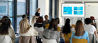 Salle de classe avec des étudiantes assistant à une présentation projetée sur un écran