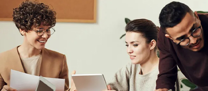 Trois jeunes collègues souriants consultant des documents et une tablette
