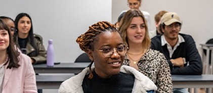 Étudiante souriante à lunettes assise en classe parmi d'autres étudiants