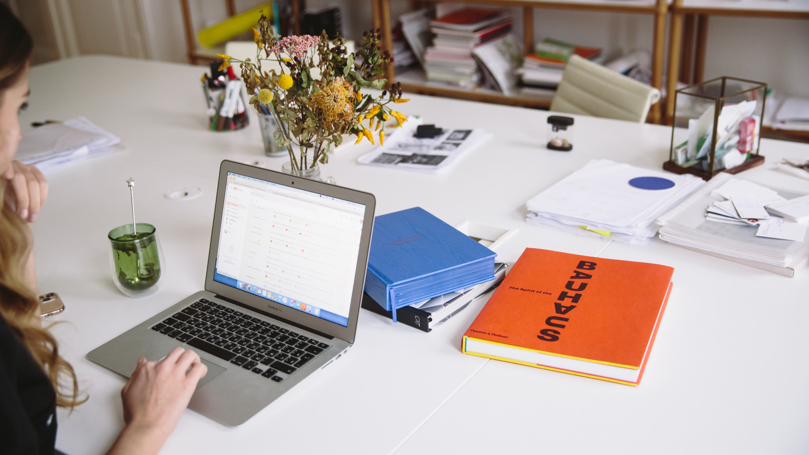 Personne travaillant sur un ordinateur portable à une table encombrée de classeurs et de livres