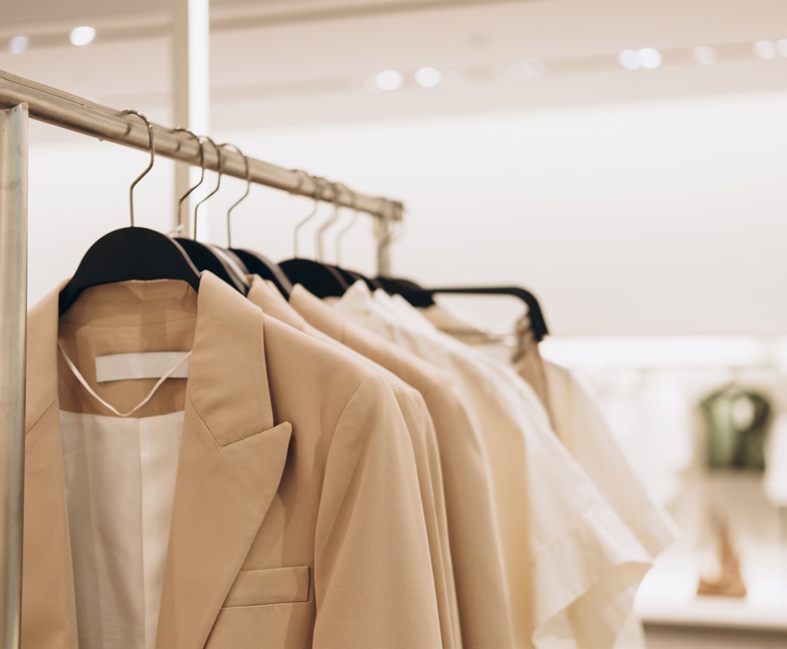 A rail of neutral-toned tailored jackets and shirts in a bright retail store