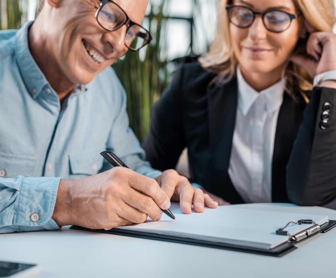 Two colleagues smiling as they review and sign a document together at a desk
