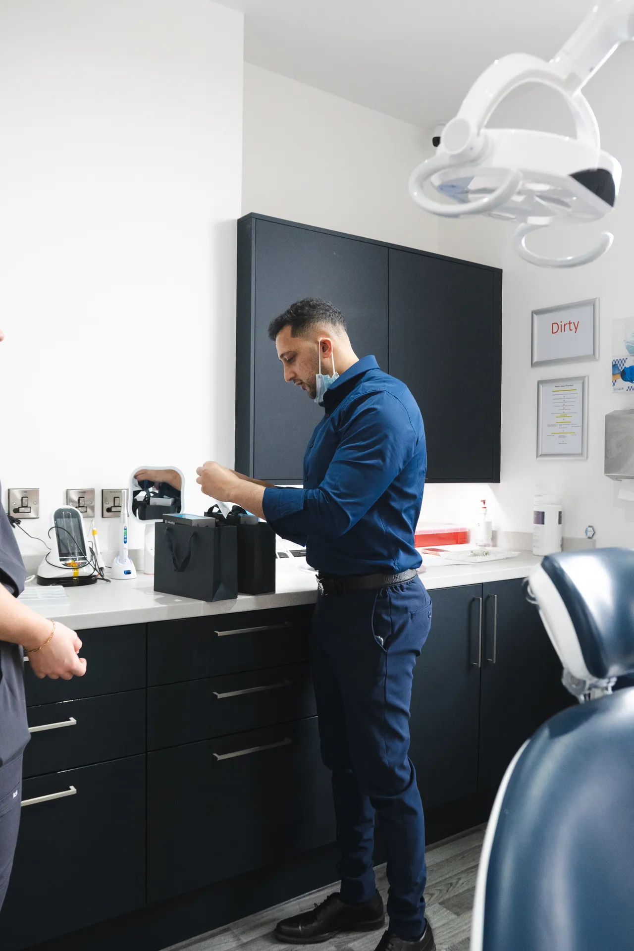 Man in blue shirt standing at a dental office counter with dental equipment and cabinets.