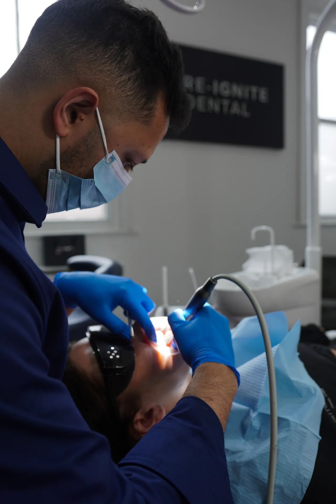 Dentist wearing a mask and blue gloves performing a dental procedure on a patient lying in a dental chair.