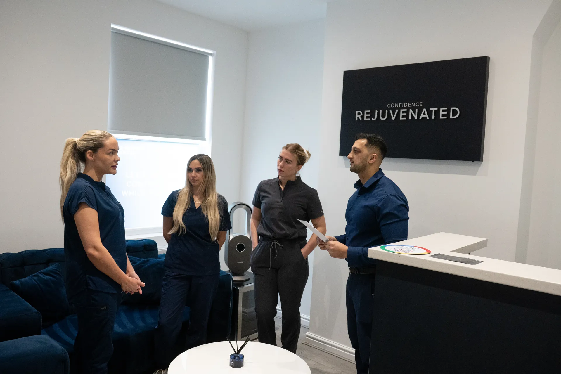 Four medical professionals in discussion in a modern office with a sign reading Confidence Rejuvenated.