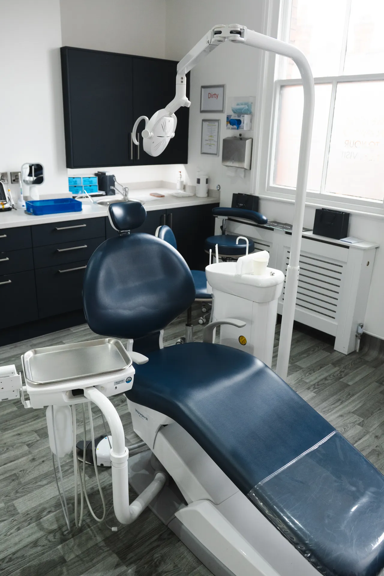 Modern dental exam room with blue dental chair, overhead light, and cabinetry.