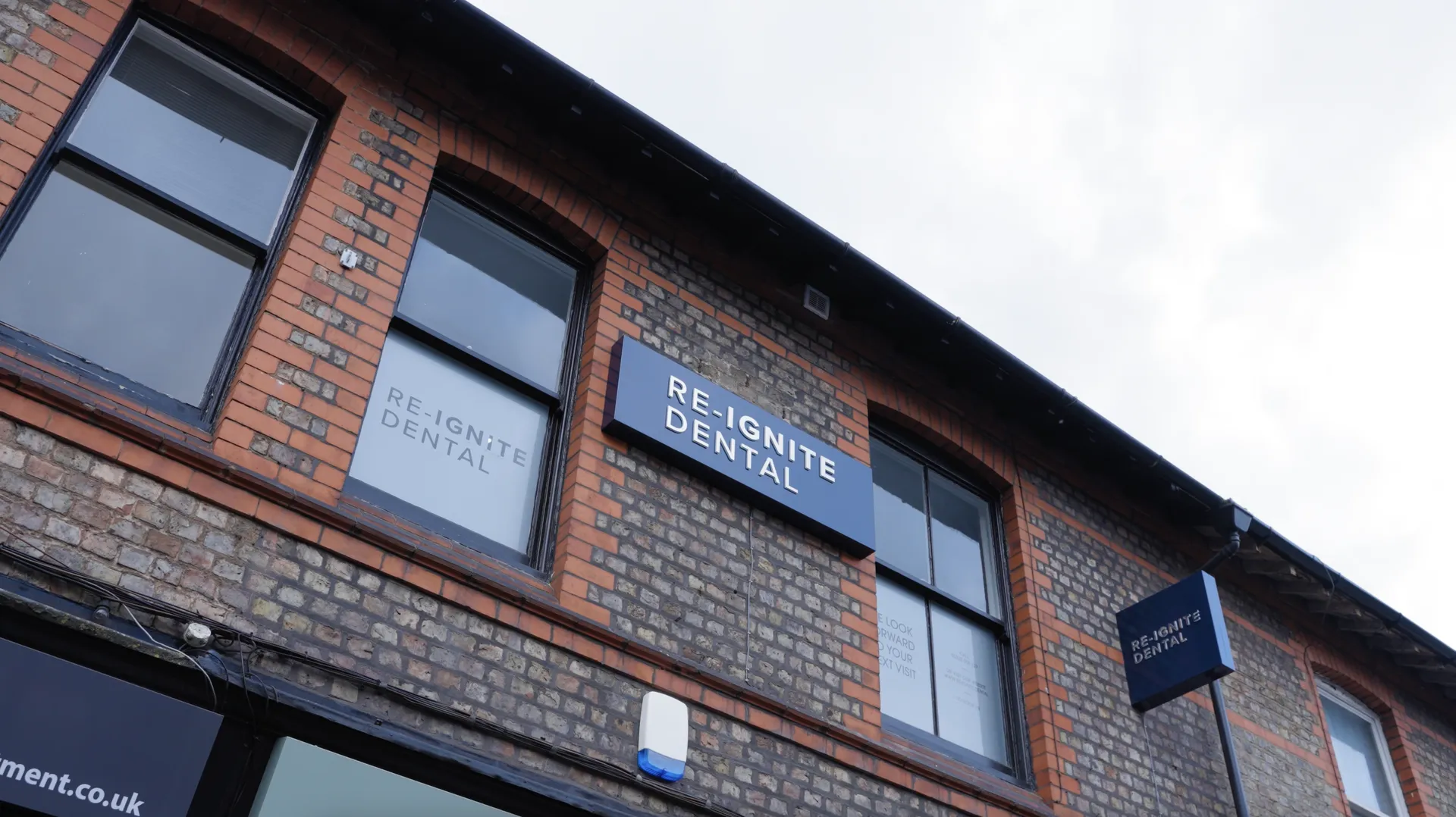Brick building with signage for Re-Ignite Dental on windows and two blue signs.