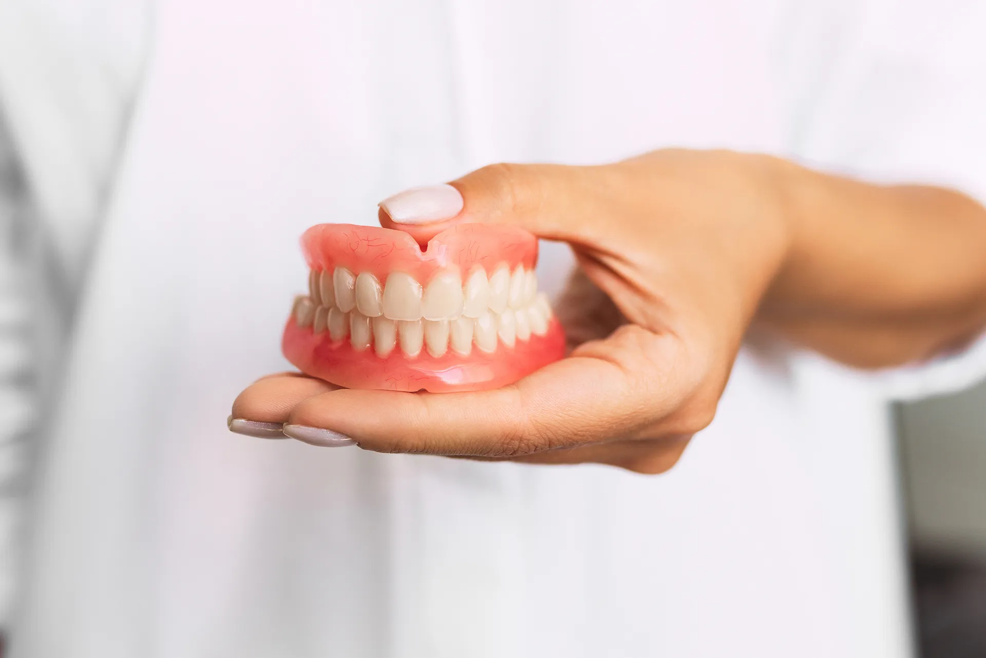 Close-up of a hand holding a set of full pink dentures with white teeth.