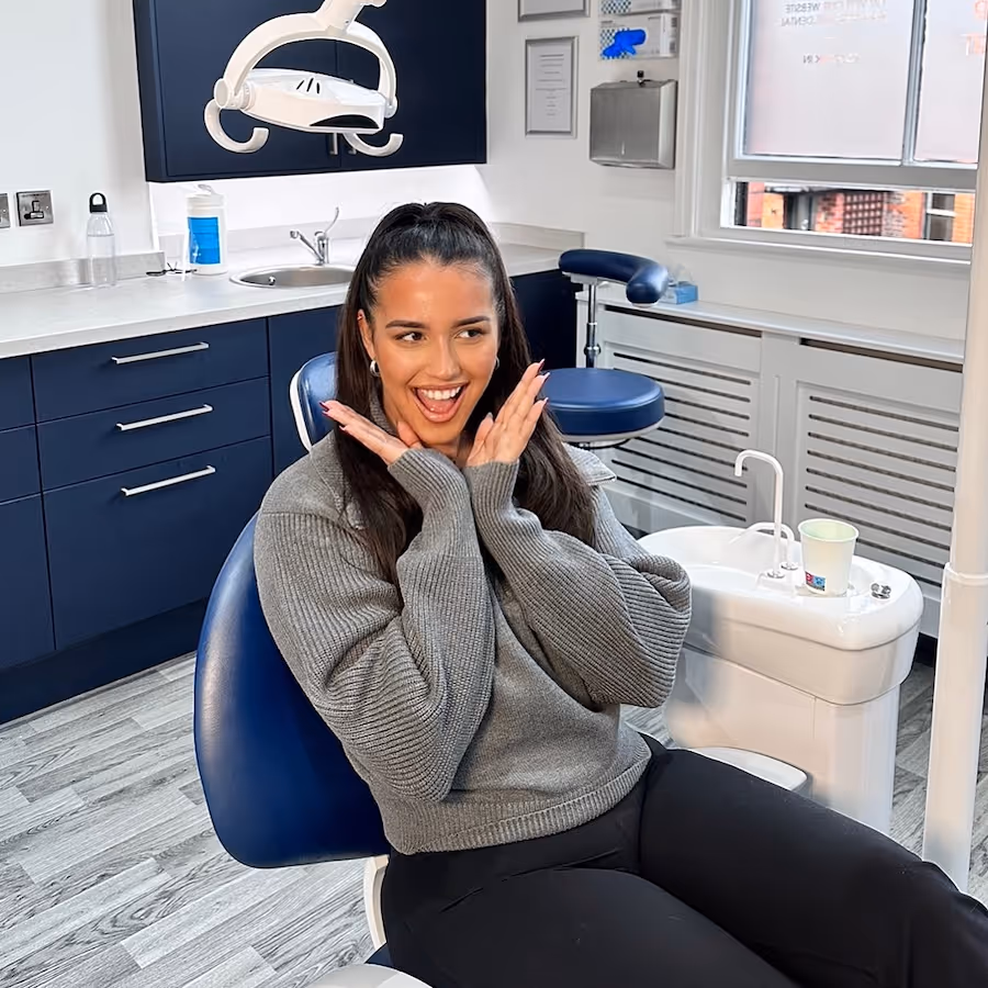 Smiling woman in gray sweater sitting in a dental chair inside a modern dental clinic.