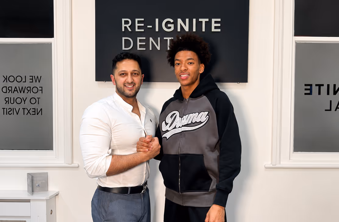 Two men smiling and clasping hands in front of a sign reading 'RE-IGNITE DENTAL'.