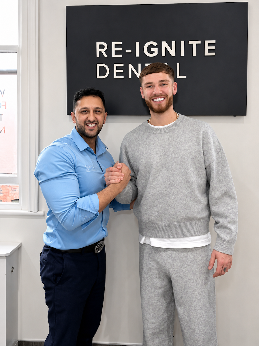 Two men smiling and clasping hands inside a dental office under a Re-Ignite Dental sign.