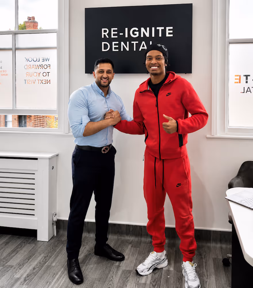 Two men shaking hands inside a dental office with a Re-Ignite Dental sign behind them.