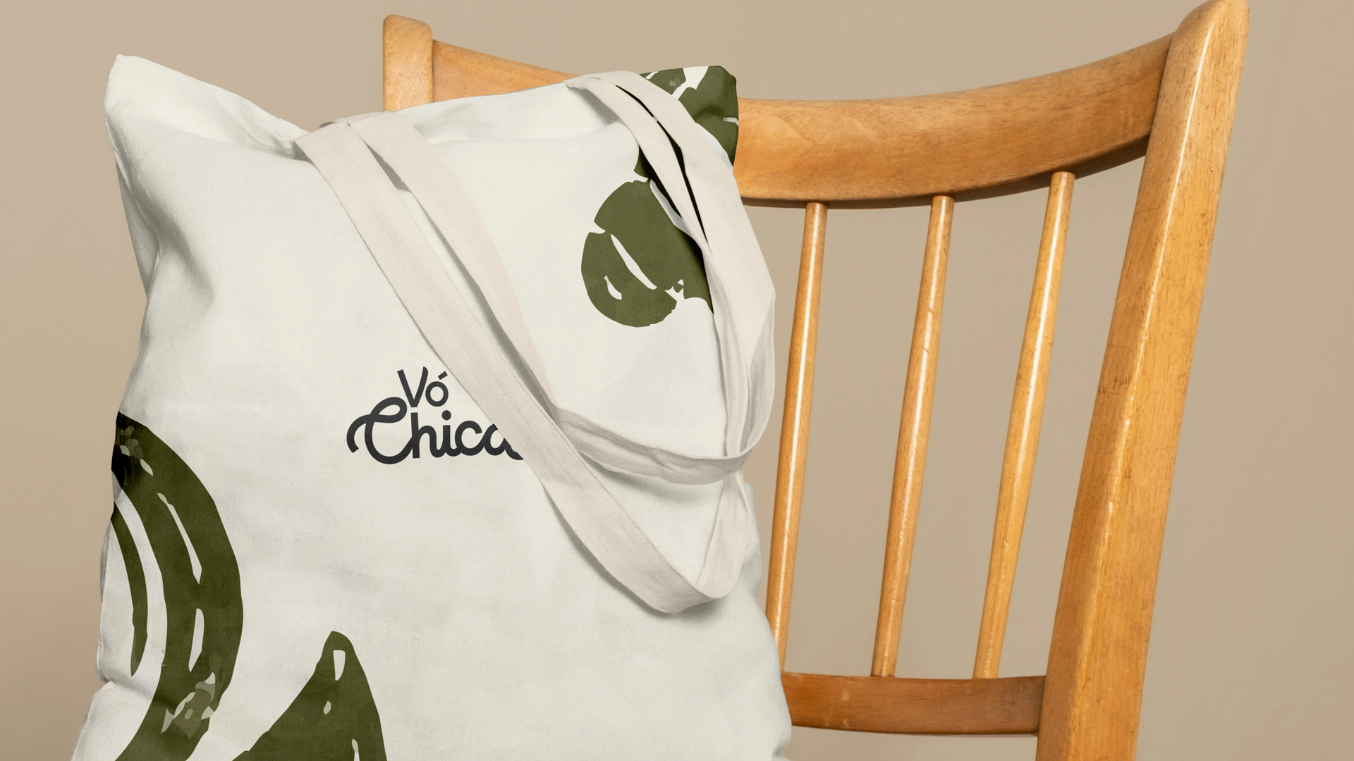 Off-white tote bag with green abstract prints and Vó Chica text resting on a wooden chair.