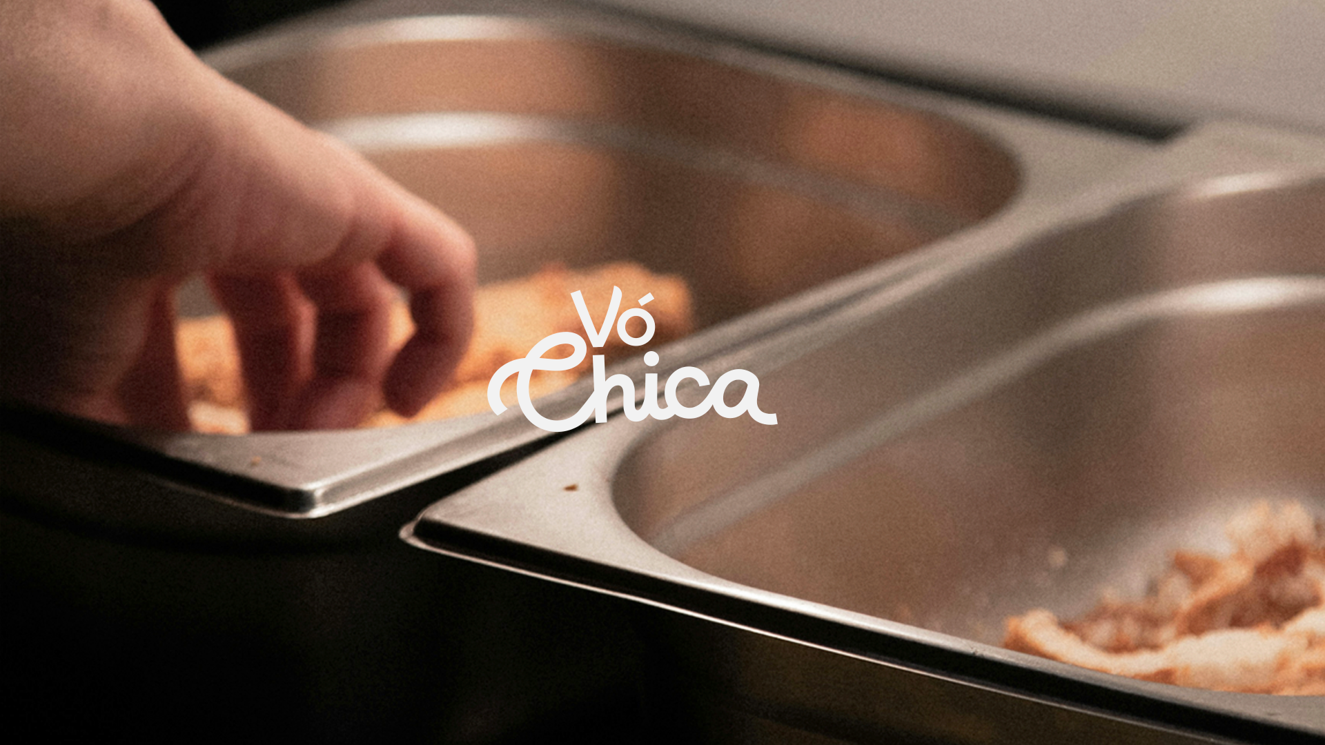 Hand reaching into a metal food tray containing fried food pieces, next to another tray with food.