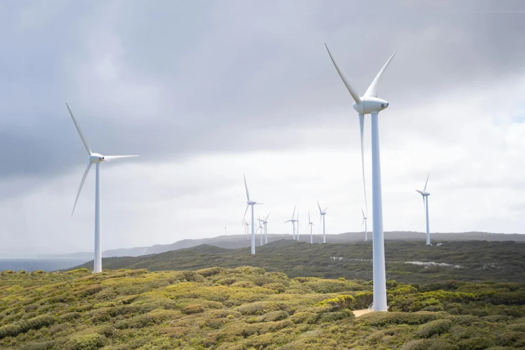 Wind turbines standing across a wide, green landscape under a cloudy sky