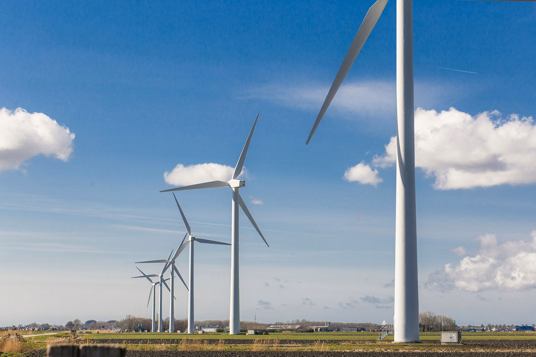 Row of tall white wind turbines in a field under a blue sky with white clouds.