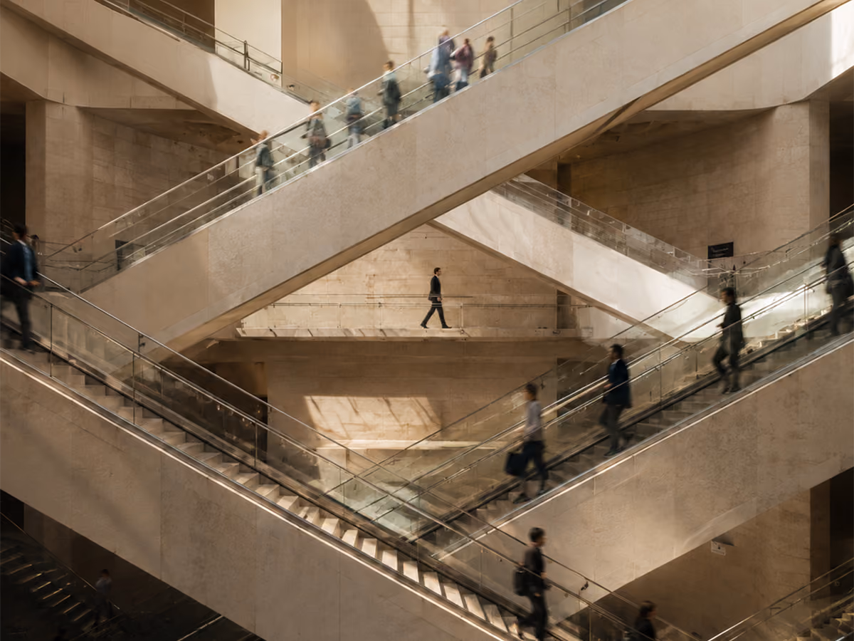 People walking up and down multiple intersecting escalators in a modern building with beige walls and soft lighting.