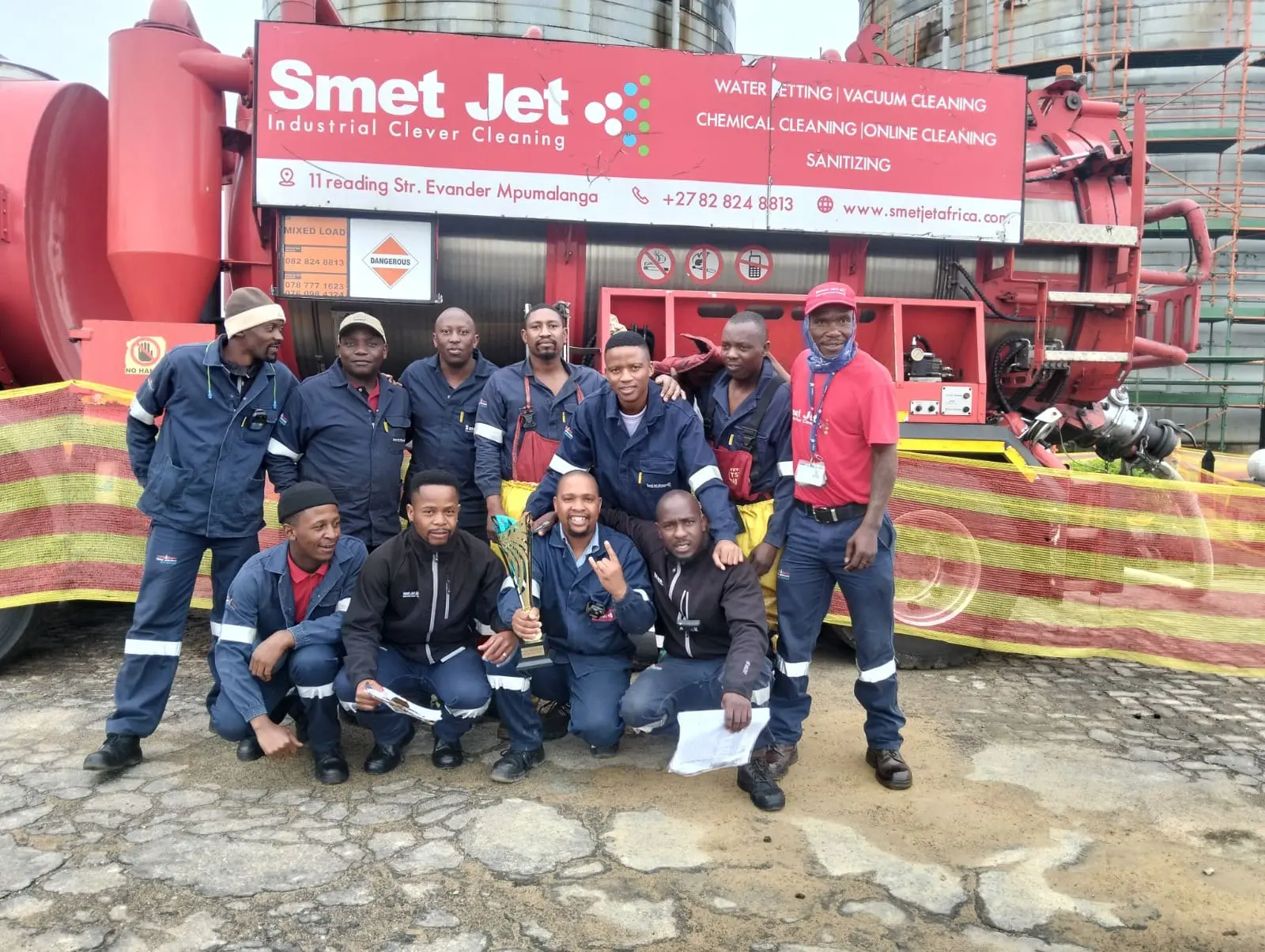 Smet Jet industrial cleaning team posing with trophy in front of red cleaning equipment and barrier.