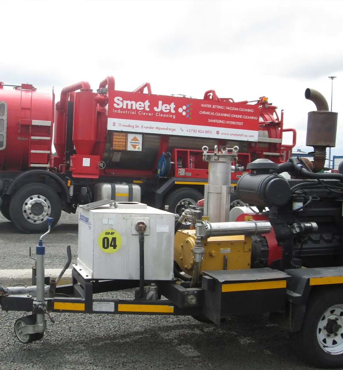 Red industrial cleaning truck labeled Smet Jet with pipes and equipment on gravel surface.