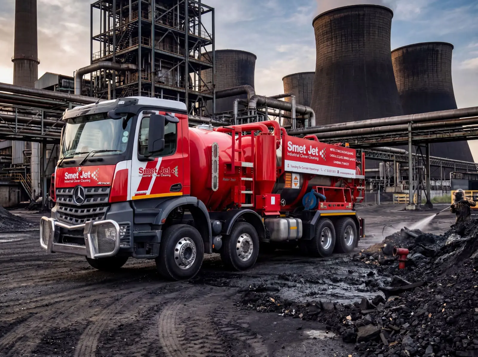 Red Smet Jet industrial cleaning truck in an industrial site with cooling towers and pipes in background.