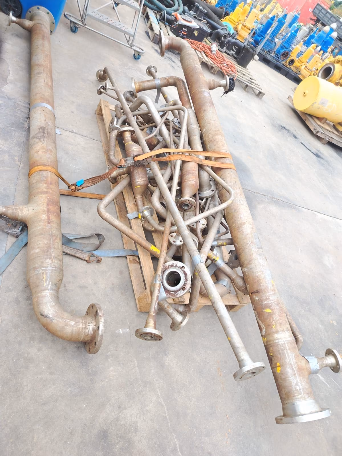 Bundle of metal industrial pipes and tubes with flanges on a wooden pallet in a workshop.