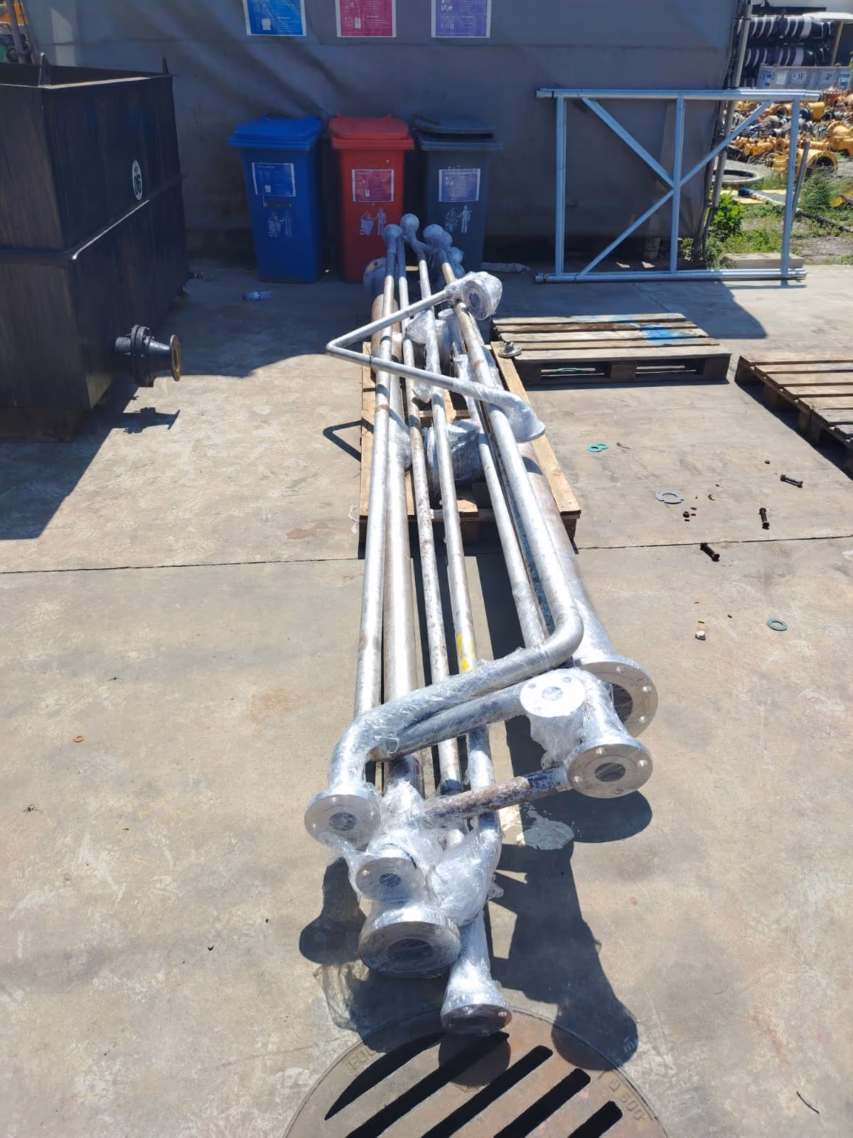 Long metal pipes wrapped in plastic lying on pallets on a concrete floor outside.