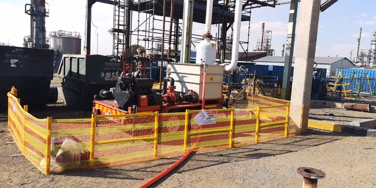 Industrial chemical cleaning setup with equipment surrounded by yellow and orange safety fencing outdoors.
