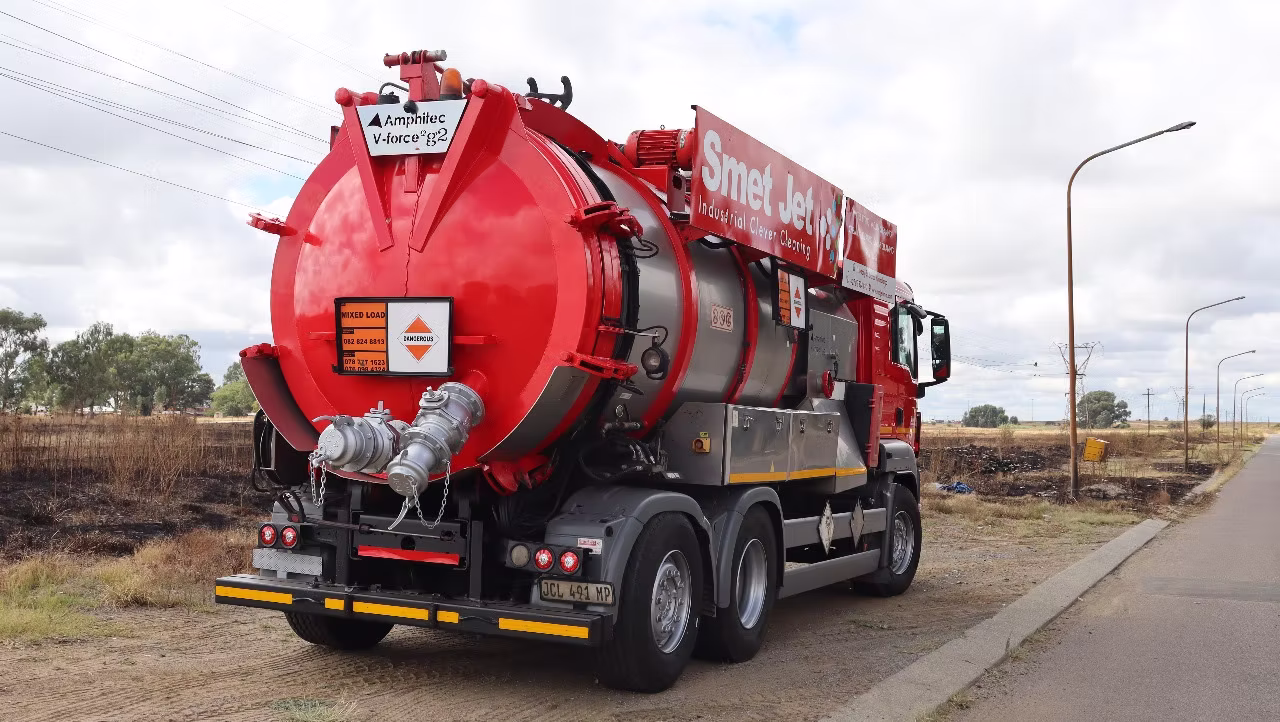 Red and silver industrial vacuum truck parked beside a road on a cloudy day.