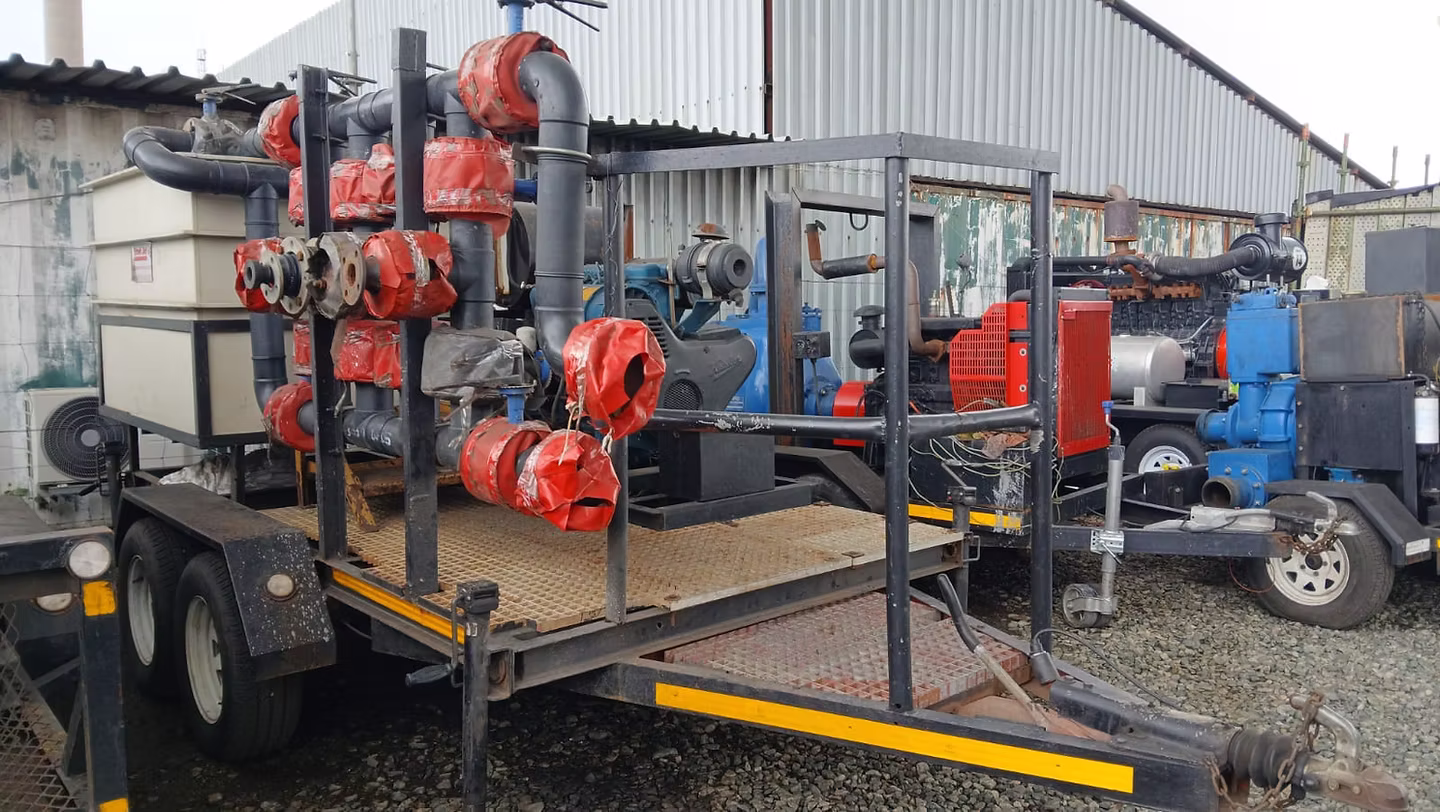 Industrial trailer with black and red insulated piping and pumps on a gravel lot outside a warehouse.