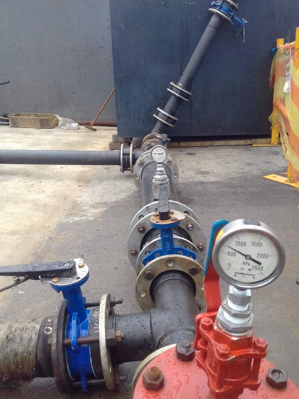 Close-up of a black pipeline system with valves and pressure gauges on a wet surface.