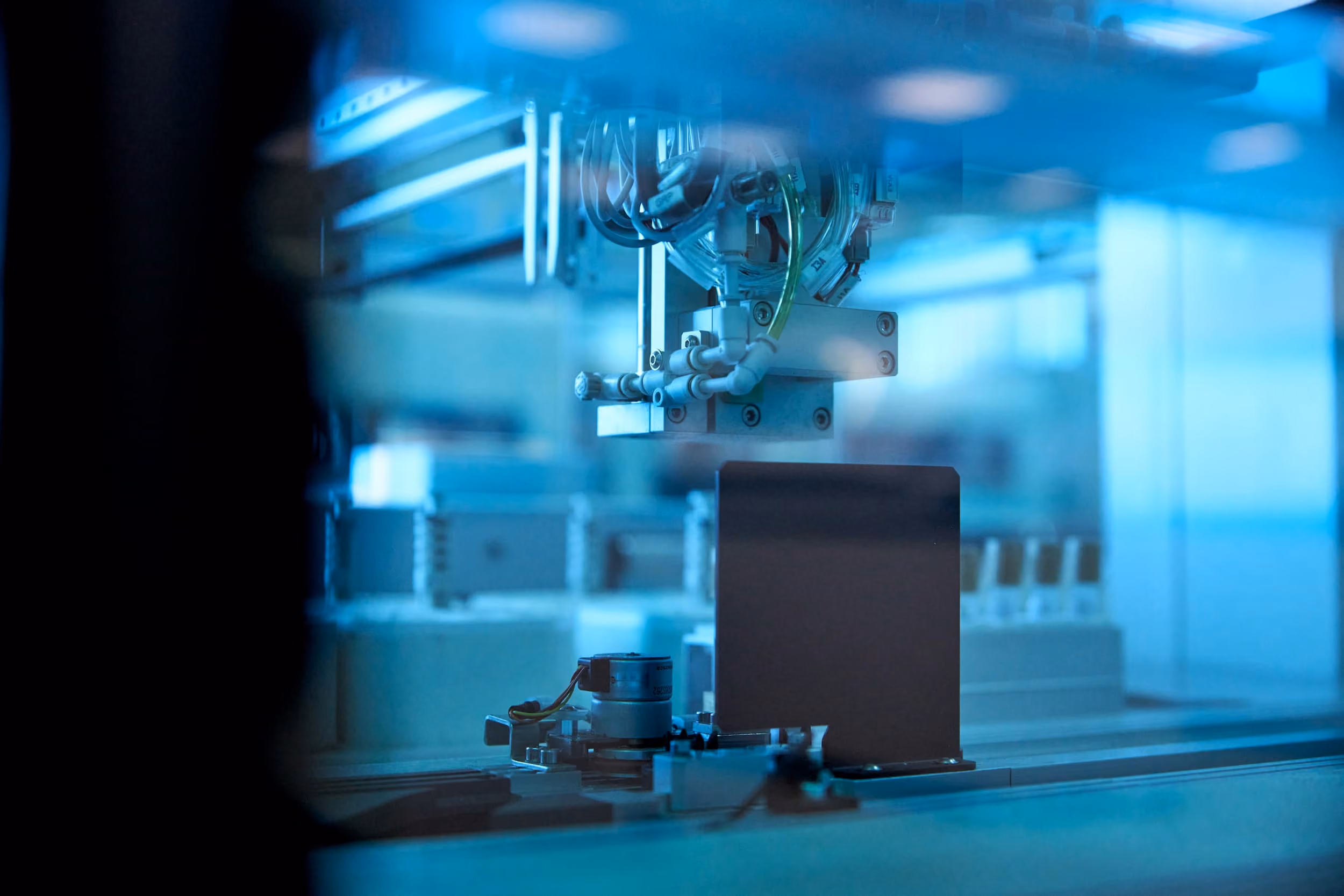Vue rapprochée d'une machine automatisée dans un environnement industriel avec des composants métalliques et des câbles, éclairée par une lumière bleue.