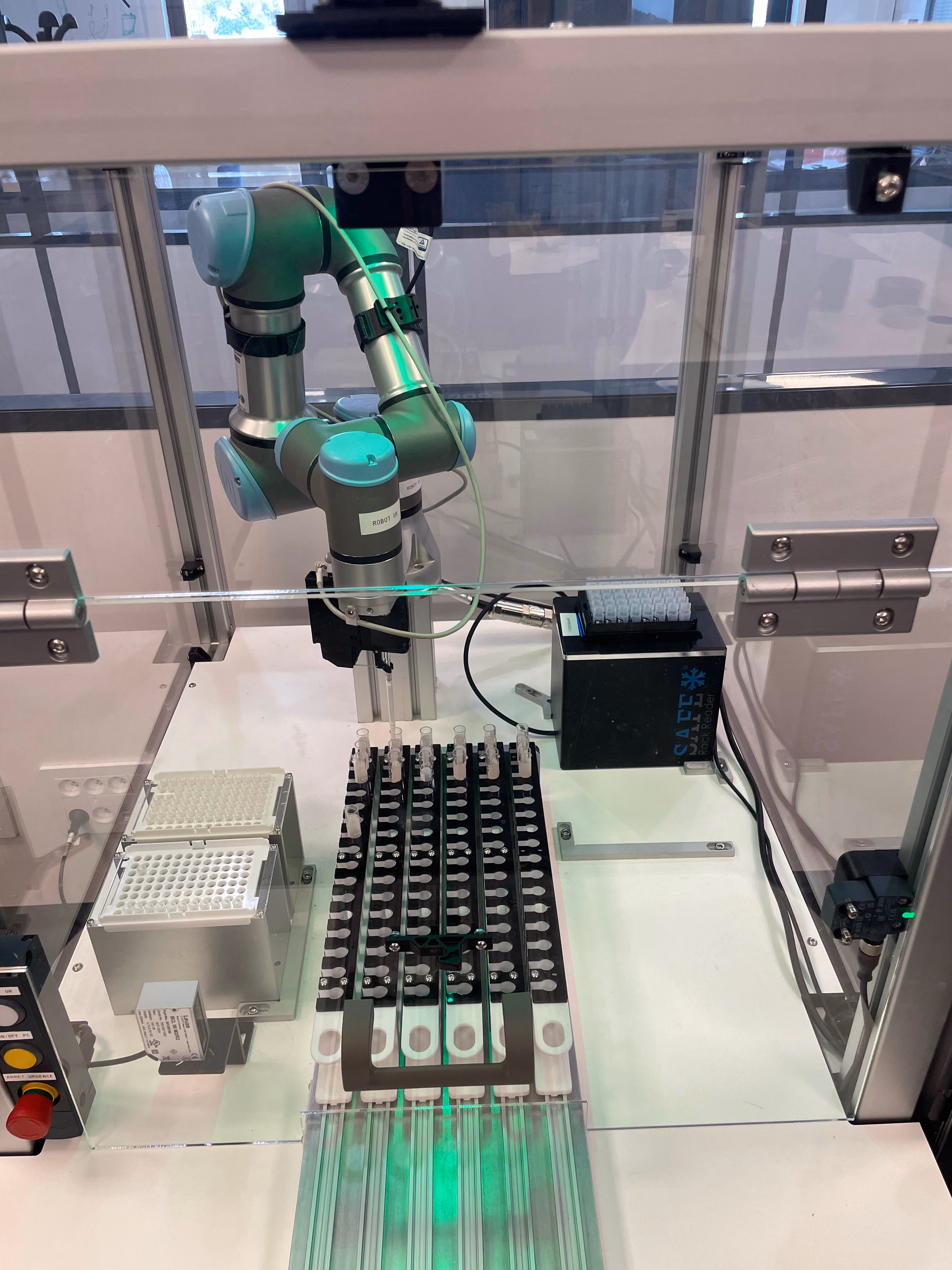 Robot collaboratif à bras articulé travaillant avec des plaques de microtubes dans une enceinte protégée en verre, utilisé pour des manipulations automatisées en laboratoire.
