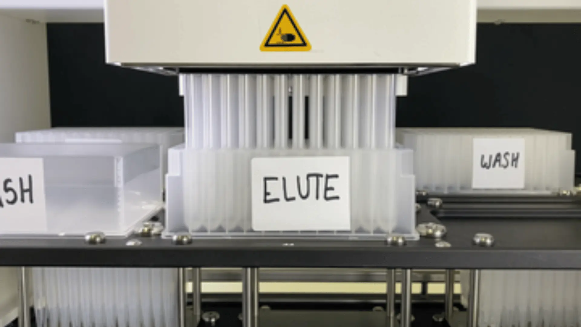 Vue rapprochée d'un dispositif automatisé de purification des protéines avec des tubes en plastique étiquetés ELUTE et WASH disposés dans un support métallique.