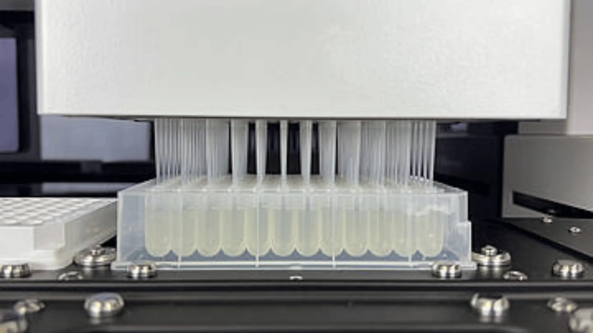 Machine de laboratoire automatisée utilisant plusieurs micropipettes pour transférer des liquides transparents dans une rangée de tubes en plastique transparents.