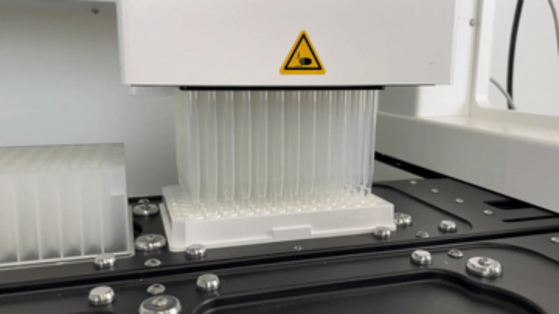Machine automatisée avec de nombreuses micropipettes alignées, utilisée pour des essais biologiques en laboratoire.