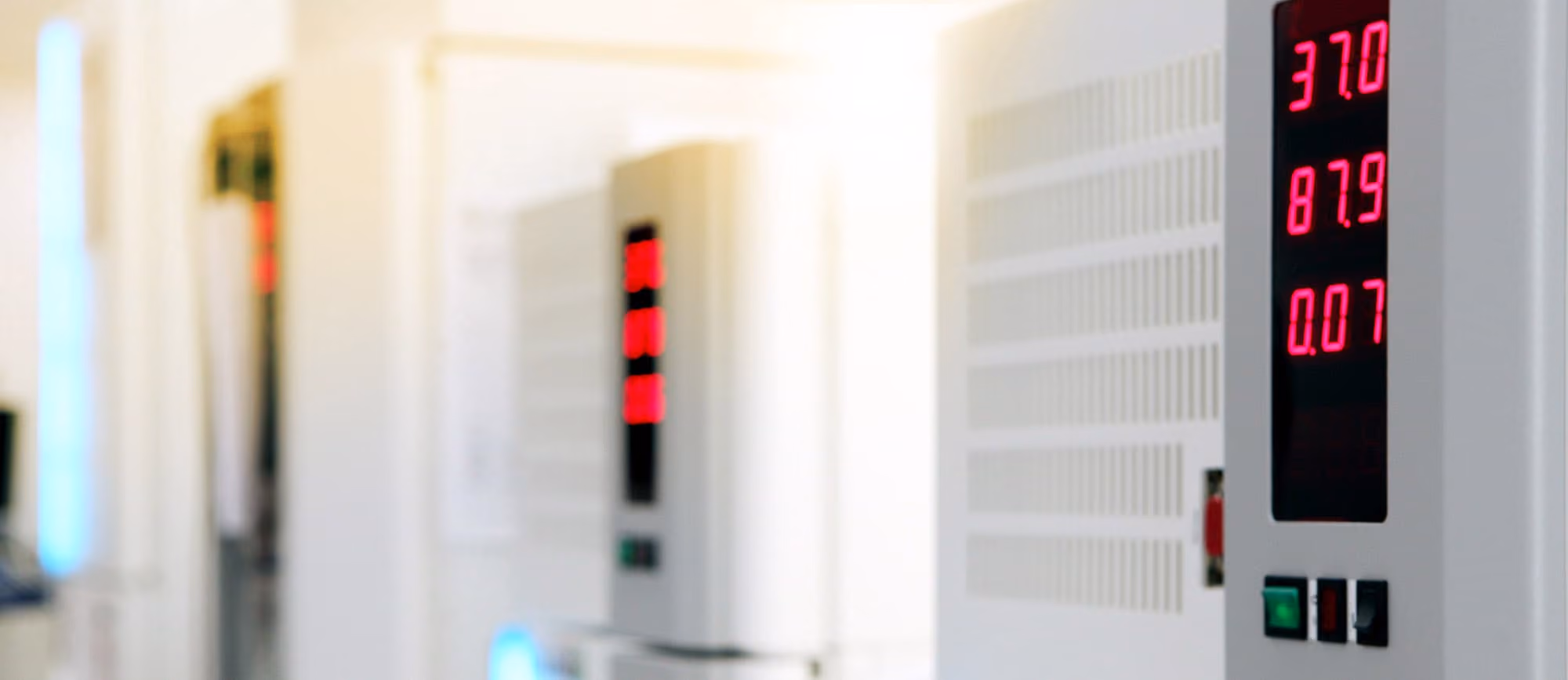 Affichage numérique en rouge sur un équipement électrique blanc indiquant les valeurs 37.0, 87.9 et 0.07, avec des interrupteurs en dessous, dans un environnement lumineux et flou en arrière-plan.