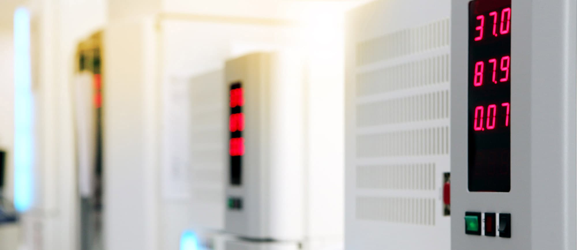 Affichage numérique en rouge sur un équipement électrique blanc indiquant les valeurs 37.0, 87.9 et 0.07, avec des interrupteurs en dessous, dans un environnement lumineux et flou en arrière-plan.
