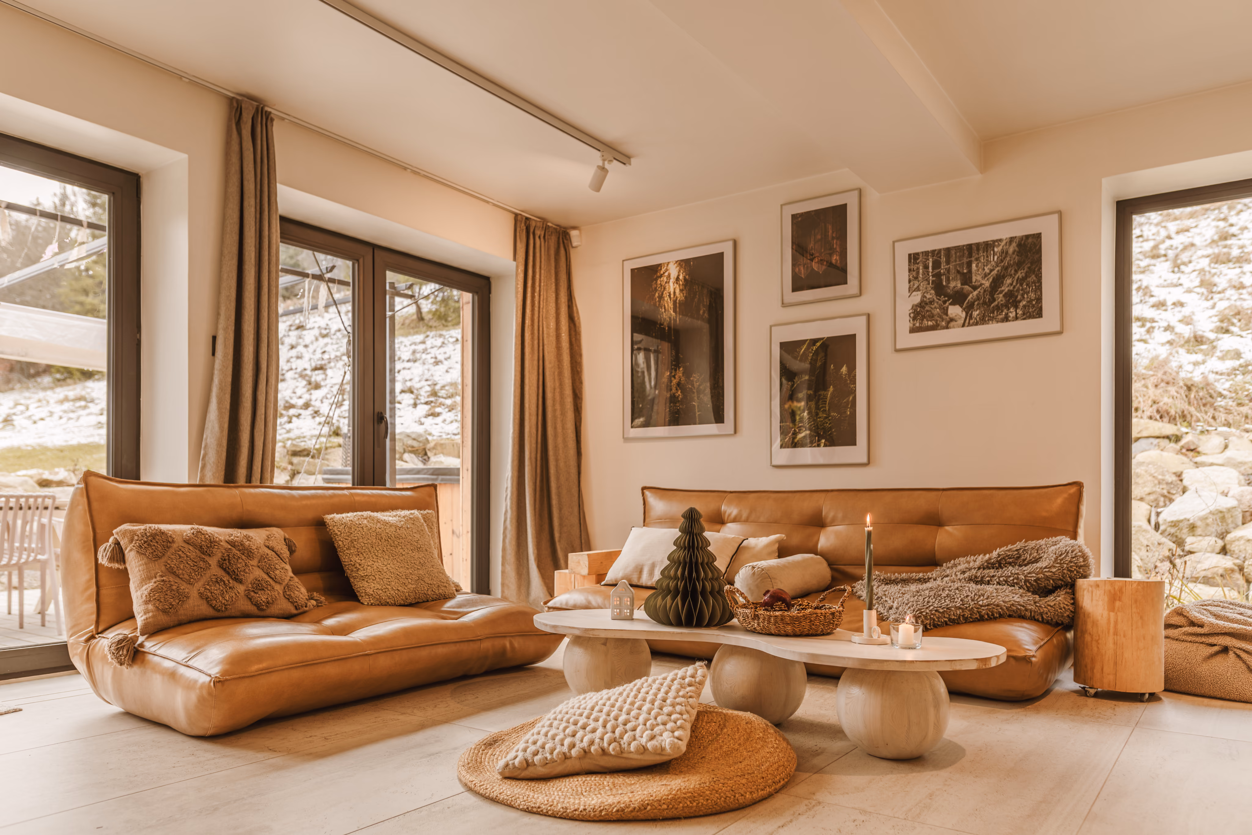 Cozy living room with tan leather sofas, white coffee table, cushions, candles, and forest-themed wall art.