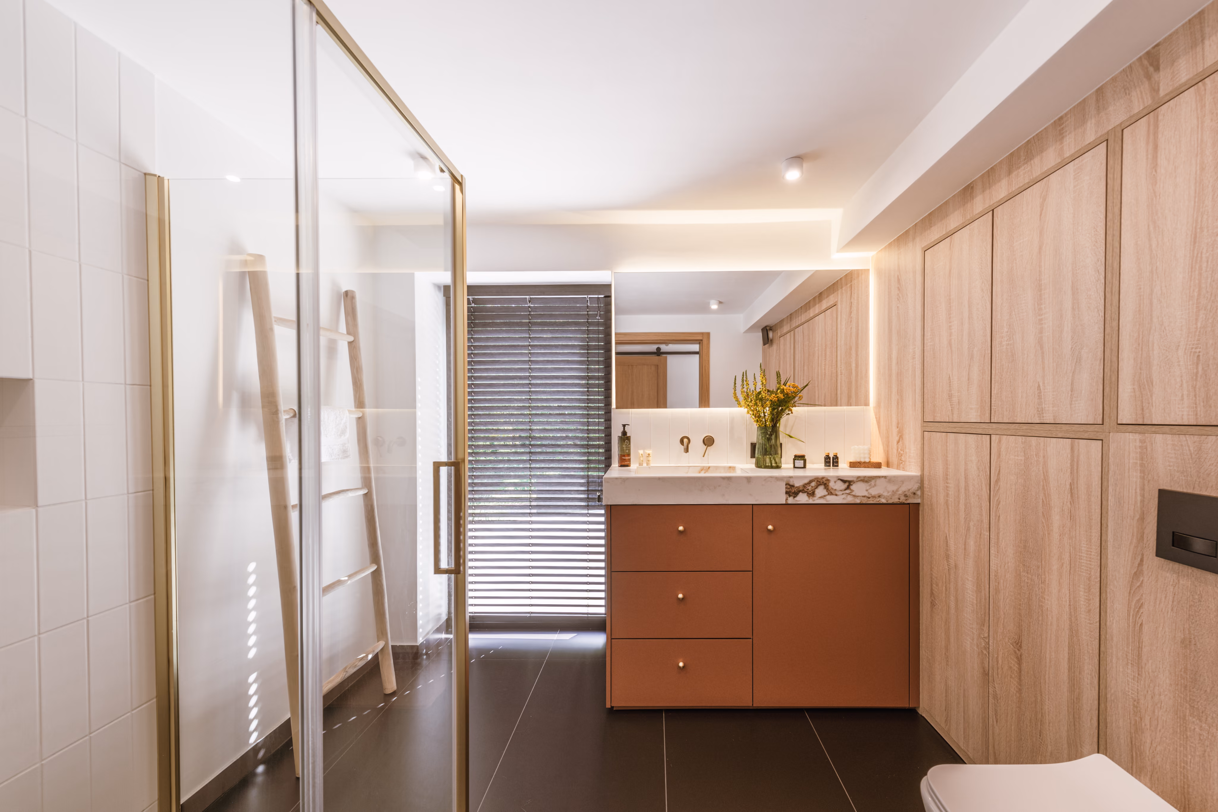 Modern bathroom with glass shower, wooden ladder towel rack, brown vanity, and large mirror.