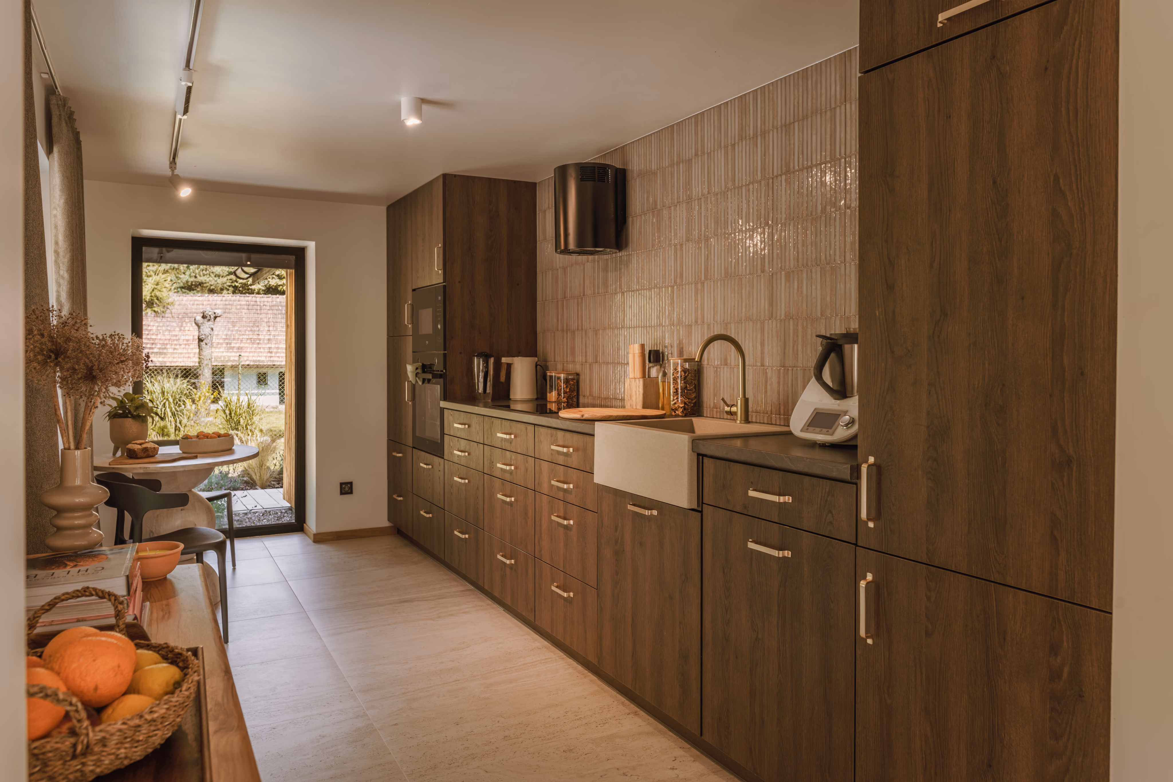Modern kitchen with wood cabinets, beige tiled backsplash, farmhouse sink, and light gray floor tiles.