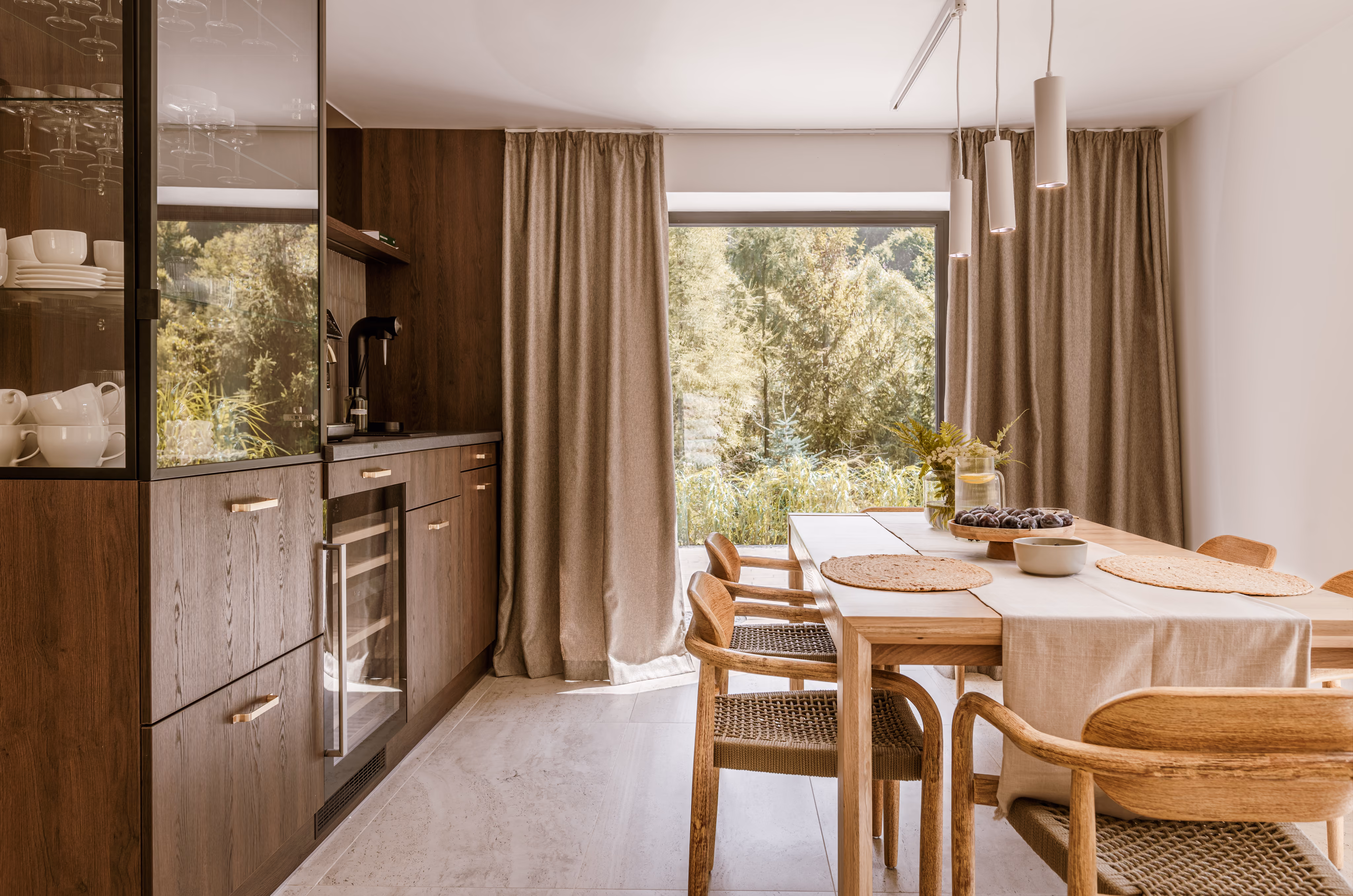 Modern dining area with wooden table, woven chairs, pendant lights, and a large window with nature view.