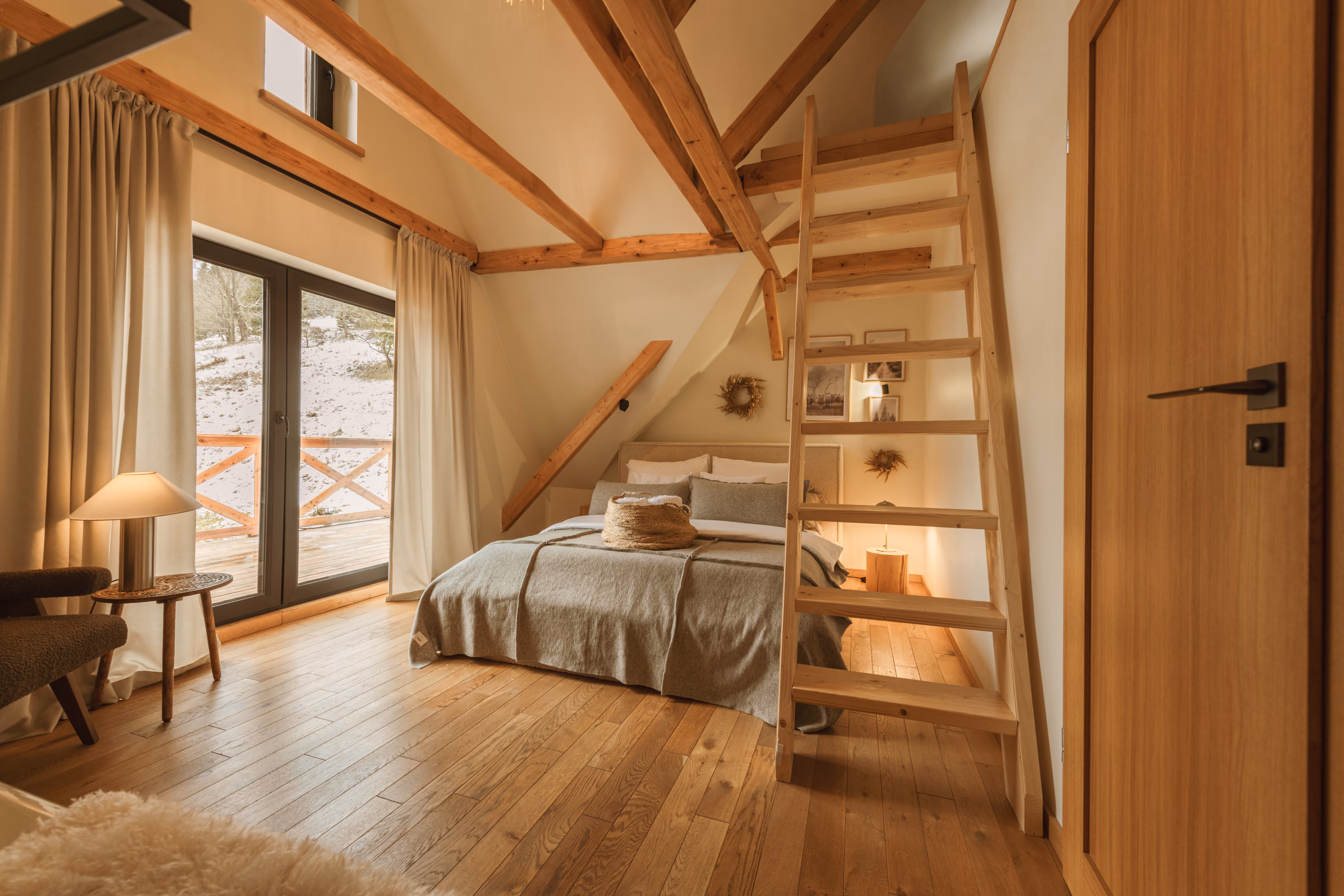Cozy attic bedroom with wooden floor, slanted ceiling, bed, ladder loft, and large glass door to snowy outdoors.